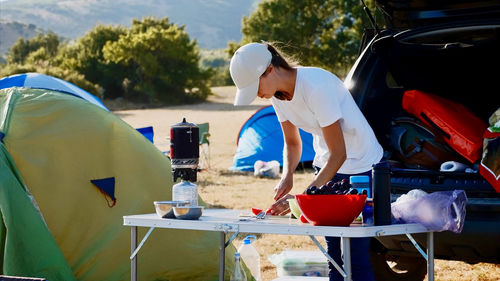 Woman preparing food while standing against car outdoors