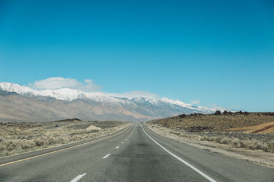 Empty road amidst landscape against clear blue sky