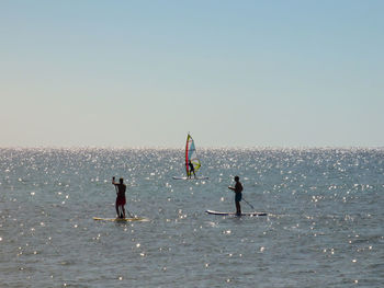 Silhouette men paddleboarding and windsurfing on sea against sky