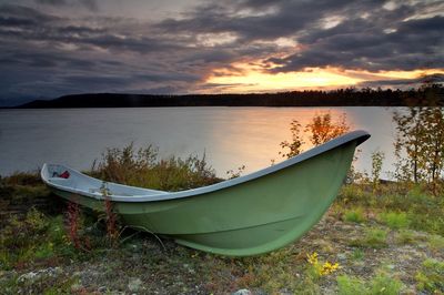 Boat moored on shore against sky during sunset