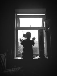 Rear view of boy standing against window at home
