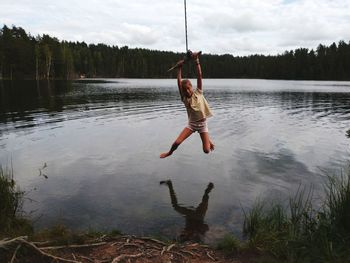 Full length of girl swinging over lake against cloudy sky in forest
