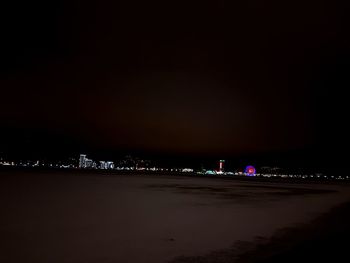 Illuminated city by sea against sky at night