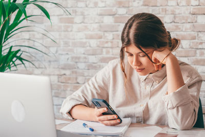 Young woman using mobile phone while sitting on table