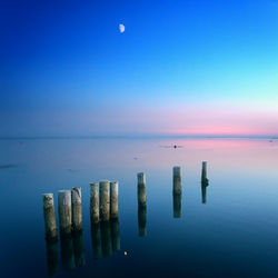 Wooden posts in sea against sky at night