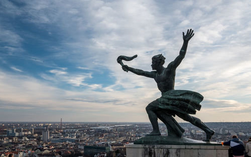 Statue in city against cloudy sky