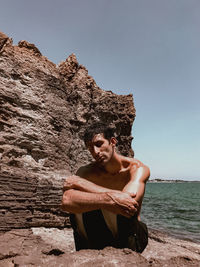 Young man on rock against clear sky