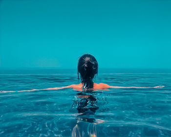 Rear view of woman swimming in infinity pool against clear blue sky