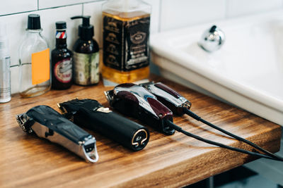 Collection of professional electric clippers near bottles of cosmetic products and washbasin in bathroom of barbershop