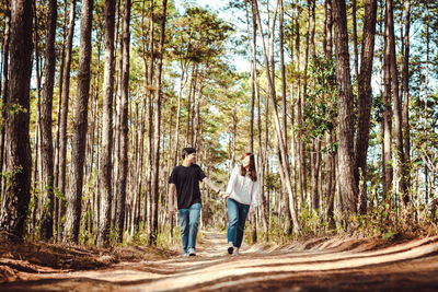 Full length of couple walking on road amidst trees in forest