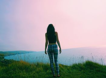 Rear view of woman standing on field by sea against sky