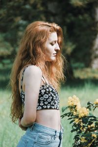 Side view of woman standing by flowering plants against trees