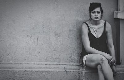 Portrait of young woman sitting against wall
