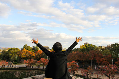 Rear view of woman with arms raised sitting against sky