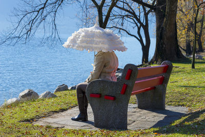 Rear view of woman sitting on bare tree against sky