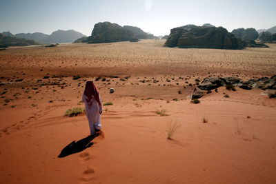 Rear view of man walking on sand dune against clear sky