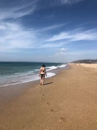 Rear view of woman walking at beach against sky