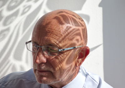 Close-up of man wearing eyeglasses against wall