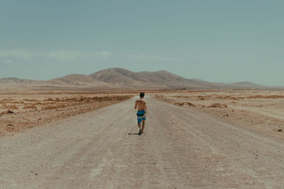 Rear view of shirtless man walking on dirt road at desert