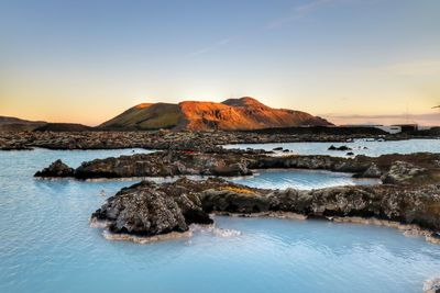 View of rocks in calm sea at sunset