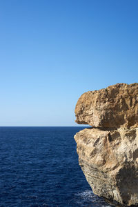 Stack rock in sea against clear blue sky