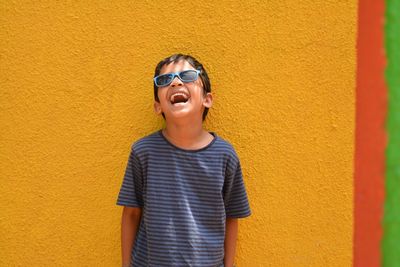 Happy boy laughing against yellow wall