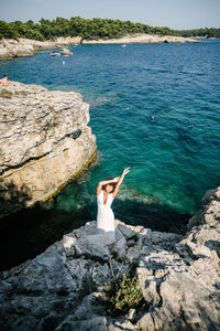 High angle view of woman with arms raised standing on cliff against sea