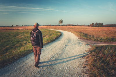 A man with a backpack goes gravel road on an autumn day