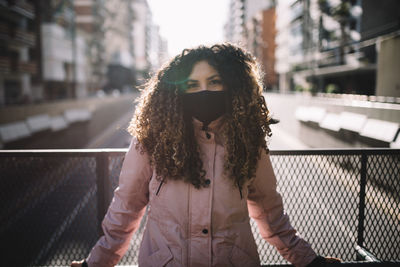 Portrait of young woman standing by railing in city