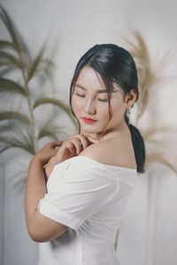 Young woman looking down while standing against wall