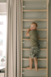 Full length portrait of boy with down syndrome climbing on ladder at home
