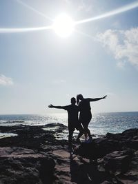 Silhouette people enjoying in sea against sky on sunny day