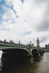 Arch bridge over river against cloudy sky