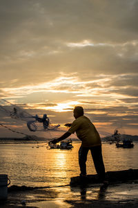 Fisherman throwing net at jetty during sunset