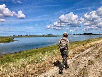 Rear view of a woman walking at a rural road along a lake with a blue sky with white clouds above