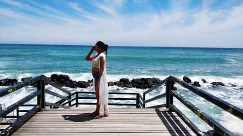 Young woman standing on a dock against blue sea and sky