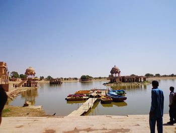 Boats in river by temple against clear sky