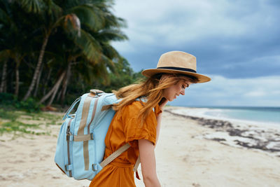 Woman wearing hat standing at beach against sky
