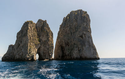 Rock formation in sea against clear sky