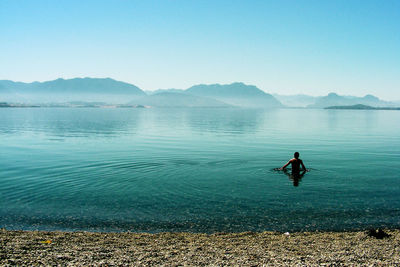 Rear view of man swimming in lake against clear sky