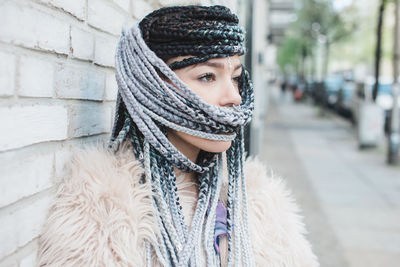 Beautiful woman with braided hair standing against wall