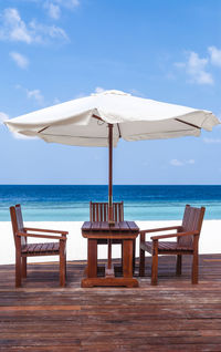 Chairs and table on beach against sky