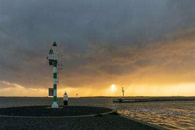 Lighthouse by sea against sky during sunset