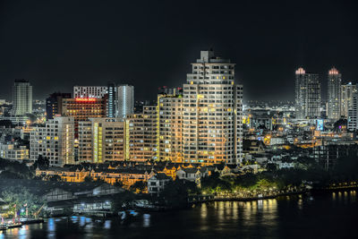 Illuminated buildings by river against sky in city at night