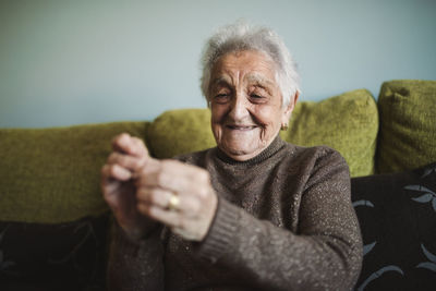 Portrait of smiling senior woman sitting on couch passing thread through buttonhole of sewing needle