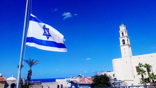 Low angle view of flags on building against blue sky