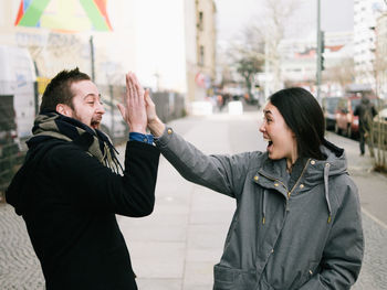 Excited friends giving high-five on sidewalk in city