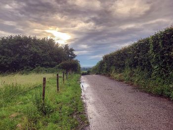 Road amidst trees on field against sky