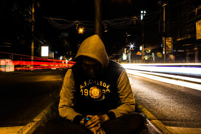 Rear view of man sitting on road at night