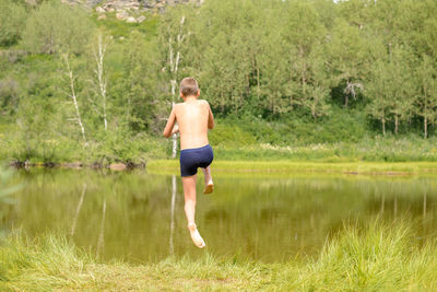 Full length rear view of shirtless boy jumping in lake